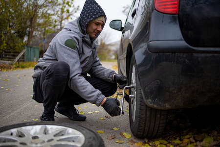 The driver changes the wheel of the car. Change summer wheels for winter.