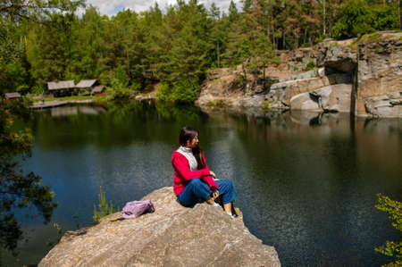 Young Adult Asian Woman with a backpack On A Rock Admiring The View Of A Lake In Autumn.の写真素材