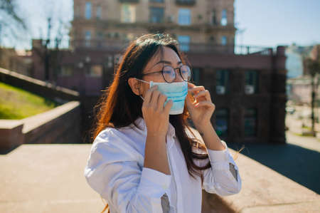 Asian Woman Waiting For Bus At Bus Stop In City Street And Wearing Face Medical Maskの写真素材