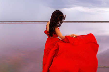 Elegant Woman In Red Silky Dress Walking By A Salt fantastic Lake At Sunset.の写真素材