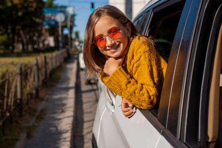 A little girl with blond hair and sunglasses looks out the car window and smiles.の写真素材