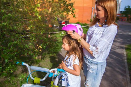 Mother puts her little daughter protective helmet for riding bike.の写真素材