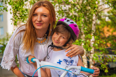 Mother puts her little daughter protective helmet for riding bike.の写真素材