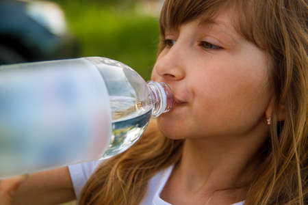 Blonde girl (7-9) drinking from water bottle, side view.