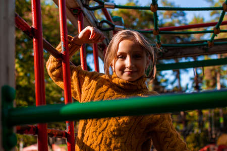 Little girl in a yellow sweater plays in the playground pulls up on the horizontal barの写真素材