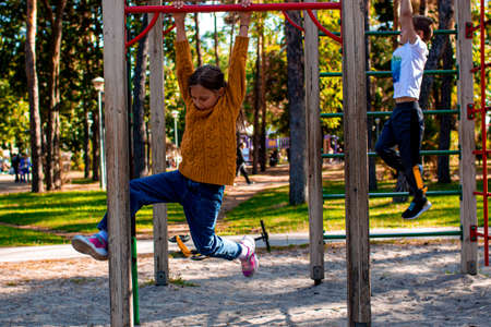 Little girl in a yellow sweater plays in the playground pulls up on the horizontal bar