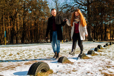 Couple in a winter forest and frozen lake. Young lovers in winter jackets laugh.