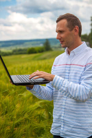 businessman with laptop and smartphone working in wheat field in blue sky background.