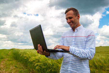 businessman with laptop and smartphone working in wheat field in blue sky background.の写真素材