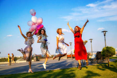Young stylish friends smiling Having Fun In City. Four beautifully dressed girlfriends laughing with balloons.の写真素材