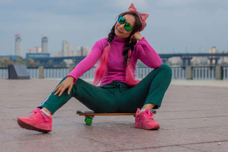 Retro asian girl in a pink sweater with a skateboard in the city