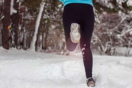 A beautiful Asian woman in a tracksuit runs with a smile in a park in winter On Snow. Winter sport in the woods in the fresh air.の写真素材