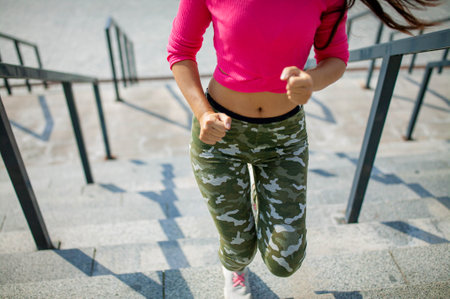 Waist up portrait of happy young asian woman training. She is listening to music from earphones and looking at smartphone. Athlete is standing outdoors and smiling.の写真素材