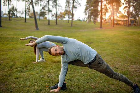 Young Couple Doing Yoga In Park Together at sunset.の写真素材