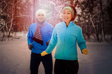 Young couple in tracksuit run and smile in the park in winter. Couple doing sport in the fresh air in the winter in the snow.の写真素材