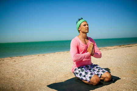 Sport man In Pink training in yoga on the beach.の写真素材