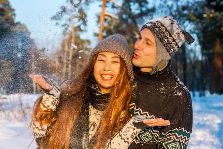 Beautiful mixed race international couple holding snowflakes and smiling in the park in the winter on the snow.の写真素材