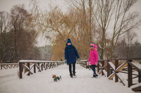 Happy cheerful family with children and dog having fun on snow in park in winter.の写真素材