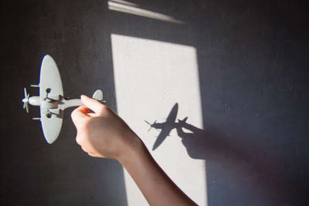 Interesting abstract background with a shadow on the concrete wall from the blinds. A hand is holding a plane and there is a shadow on the wall.の写真素材