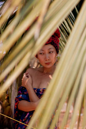 A asian woman is hiding behind palm leaves. Eastern beauty and skin care.の写真素材