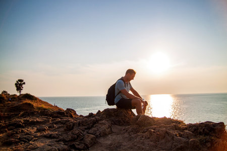 A tourist or traveler with a backpack is standing on top of a hill and admiring the beautiful view of the ocean or the sea. Walking or hiking.の写真素材
