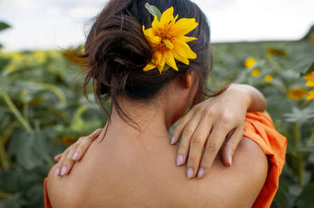 Young Beautiful Woman in evening dress In A Field Of Sunflowers Stands Back, backache concept