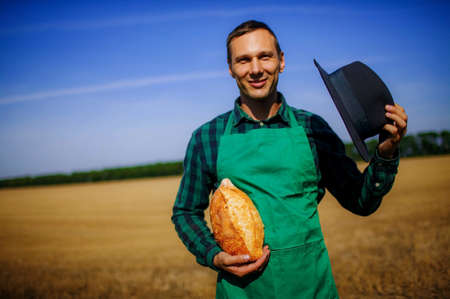 Man Farmer Holding Homemade Rustic Wheat Bread In Hands In A Wheat Field.の写真素材