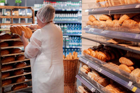 woman seller put fresh bread at bakery store shelf.