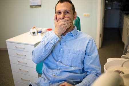 Fear Of Dentists. Phobia Dentist, Patient in the Dental Office. The young guy feels the fear of the dentist.の写真素材