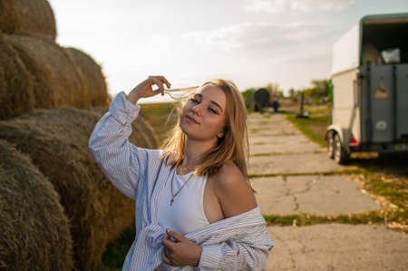 Beautiful Young Blonde Woman Standing Near Dry Hay Bale In Summer