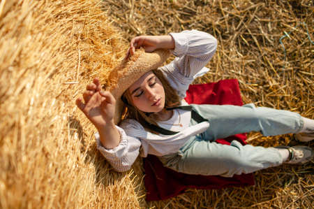 Young Beautiful Blonde Woman in a straw hat relaxing On Dry Hay In Summerの写真素材
