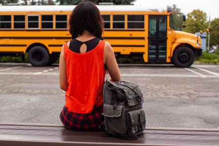 Asian Teen Girl Standing By A Big Yellow School Bus Door With Her Backpack.の写真素材