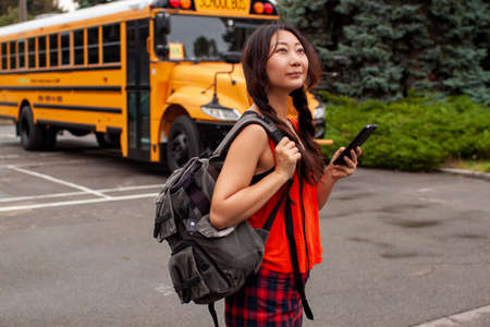 Asian Teen Girl Walking Away From School Bus While Texting On Her Phoneの写真素材