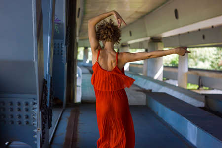 Beautiful Glamor Blonde Woman With Curly Hair In Red Dress Dancing Under The Bridge.の写真素材