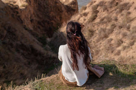 Woman Sitting On Rocks Surrounded By The Sea And Hills Covered In Greenery