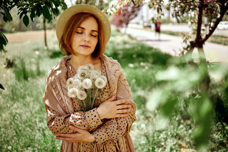 Young Beautiful Woman Holding Bunch Of Dandelion Flowers Standing On Meadow