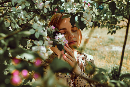 White Young Woman With Red Hair In A Pink Dress Stands By A Flowering Apple Tree.の写真素材