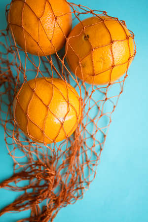 Three fresh oranges in a mesh bag On Blue Background.の写真素材