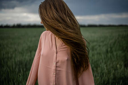Long-Haired Woman In A Pink Dress On A Green Field Before The Storm, Wind On Hair.の写真素材