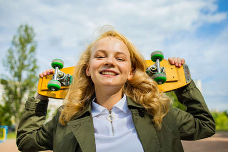 Smiling Teenage Girl With Skate Board Looking At Camera Sitting Outsideの写真素材