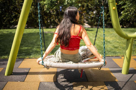 Asian Teenager Girl Sitting On Playground Swing In Summerの写真素材