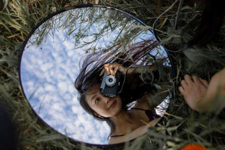 Woman Holds Camera Against A Mirror In Green Field.の写真素材
