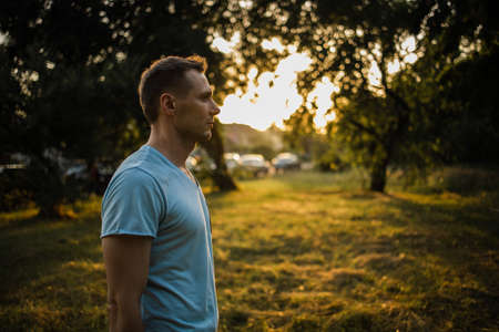 Portrait In Profile Of Young Bearded Man In Background Of Sunlight In Parkの写真素材
