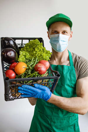 Courier with packing box with food, contactless delivery, Service quarantine pandemic virus, Volunteer woman in white protective mask and gloves delivery donation box at home.の写真素材
