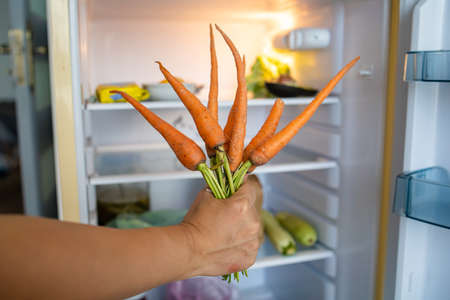 Woman's Hand Holding Bunch Of Carrots In Kitchen.