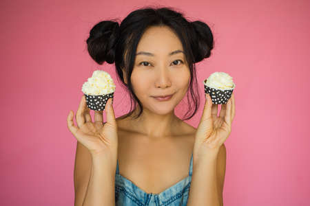 Cute Asian Girl Holds A Cupcake With Cream On Pink Background.の写真素材