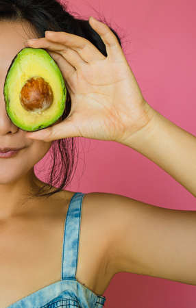 Beautiful Asian Woman Holding Avocado Half On Pink Background.