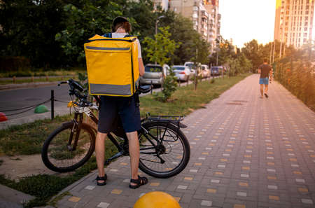 Young deliveryboy walking with orange thermal bag on city street. Man of delivery service in hurry to deliver an order. Delivery service goes to give the order quickly to the clientの写真素材