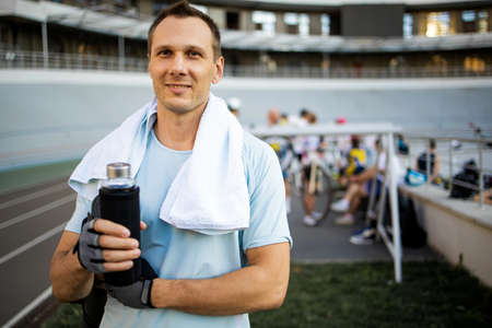 Portrait of a young man drinking some water from a bottle at the stadium and having a rest after a workout.の写真素材