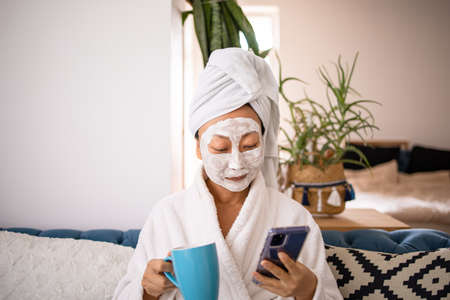 Happy surprised shocked asian woman apply facial mask and using cellphone got a good news when...